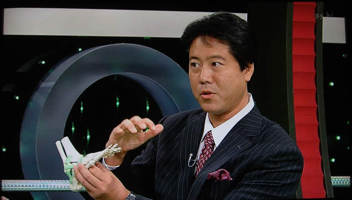 (番組キャプチャ)吉野院長が足の骨の模型を手にし、横アーチの説明を行う様子の上半身